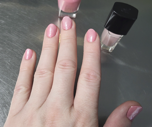 picture of fingers with glimmering pink nail polish applied over a stainless steel counter top with nail polish bottles in the background